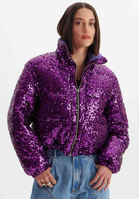 Modelo veste jaqueta puffer cropped com acabamento metalizado em paetês roxa Lança Perfume com fecho frontal em zíper metálico.